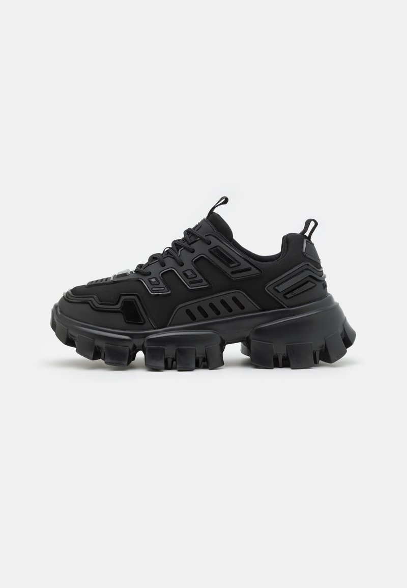 Schwarze klobige Sneaker mit dickem, robustem Profil, Schnürverschluss und strukturiertem synthetischen Obermaterial auf einem schlichten weißen Hintergrund.