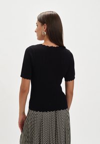 Czarny krótki top wykonany z dzianiny z falbaniastym dekoltem i wzorzystą teksturą, połączony z plisowaną spódnicą w wzory.