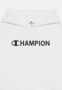 Sudadera blanca con un gran logo negro de "CHAMPION" centrado en la parte frontal. Tejido suave y texturizado con un bolsillo canguro y capucha ajustable.