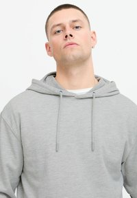 Grå hettegenser med snor, laget av et mykt stoff. Har en avslappet passform og et enkelt design uten mønstre eller detaljer.