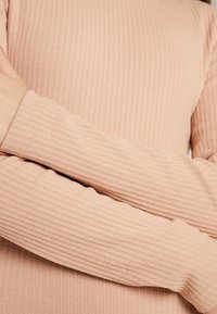 Haut ajusté à manches longues en tissu côtelé rose doux. Présente de fines rayures horizontales et des coutures précises le long des poignets.