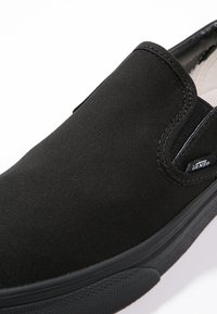 Black slip-on shoe made of canvas with a rubber sole. Smooth texture with elastic side accents and a subtle logo tag near the heel.