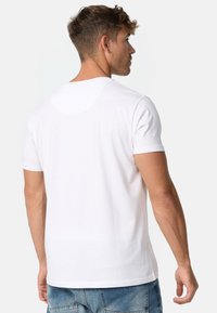 Camiseta de algodón blanca con cuello redondo y mangas cortas. La parte posterior presenta un diseño liso y sin adornos visibles.