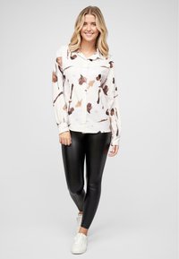 Knappskjorte med hvit bunn og abstrakt brun blomstertrykk; kombinert med svarte tights og hvite joggesko. Mykt, glatt stoff.