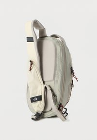 Ελαφρύ μπεζ και γκρι σακίδιο πλάτης με επενδεδυμένη πίσω επιφάνεια, ρυθμιζόμενο λουράκι, μπροστινή τσέπη με φερμουάρ και το λογότυπο The North Face στην τσέπη του λουριού.