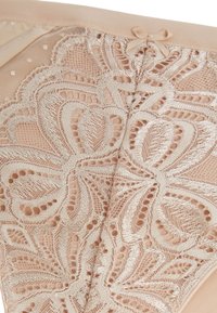 Culotte en dentelle beige avec une broderie florale complexe, une superposition de mesh transparent et un petit nœud décoratif à la taille.