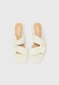 Sandales blanches à enfiler avec un design en tissu torsadé, bout carré et petit talon block, featuring une texture lisse et un style minimaliste.