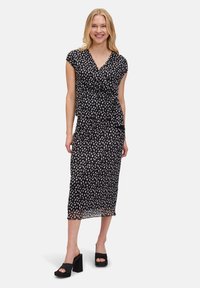 Robe noire enveloppante avec motif à pois blancs, manches courtes et jupe fluide ; assortie avec des sandales à plateforme noires. Tissu doux et léger.