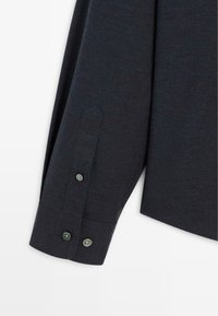 Camicetta a maniche lunghe di un blu navy scuro, caratterizzata da una texture liscia, due polsini con bottone e una vestibilità su misura con un delicato motivo a tessitura.
