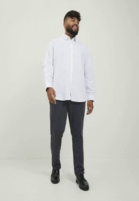 Camisa branca de manga longa com botões à frente, emparelhada com calças cinza-escuras e sapatos pretos. Tecido liso, ajuste recortado, design minimalista.