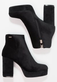 Bottines en daim noir avec un talon bloc haut, un bout arrondi et une fermeture éclair latérale. Texture lisse avec une semelle compensée pour plus de hauteur.