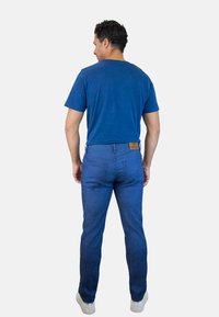 Una camiseta azul de manga corta combinada con unos jeans de color azul oscuro. Los jeans cuentan con un parche de cuero en la cintura trasera y un diseño de pierna recta.