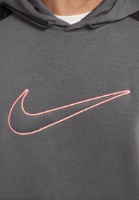 Felpa grigia con un prominente logo swoosh Nike rosa. Il materiale sembra morbido con una finitura testurizzata e include accenti neri sulle spalle.