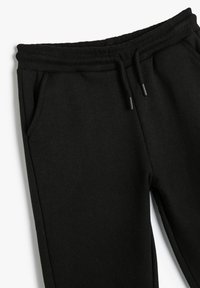 Pantalones de chándal negros con cintura elástica y cordón, con bolsillos laterales, mostrados sobre un fondo blanco.