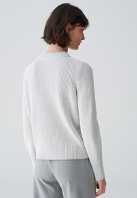 Helle graue gerippte Sweatshirt mit rundem Ausschnitt, langen Ärmeln und einer leicht verkürzten Passform, kombiniert mit grauen Hosen.