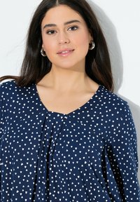 Blusa blu navy con motivi a forma di cuore bianchi, con scollo a V, pieghe sul davanti e un tessuto morbido e leggero.
