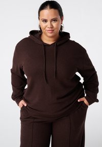 Bruine geribde hoodie met een voorzak en een trekkoord in de capuchon. Gecombineerd met bijpassende broek, die een ontspannen, losse pasvorm laat zien.