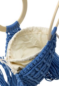 Borsa in macramè blu con anelli in legno, dotata di chiusura a cordoncino e foderata in beige. Esterno texturizzato con dettagli di frange.