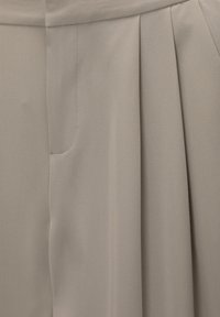 Beige geplooide stof met een gladde textuur, voorzien van een zijzak en subtiel stiksel. Het materiaal lijkt lichtgewicht en zacht.