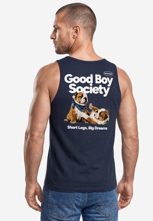 Mann trägt ein marineblaues ärmelloses Shirt mit zwei Bulldog-Welpen und dem Text "Good Boy Society, Short Legs, Big Dreams" auf dem Rücken.