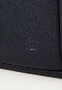 Sac à main en cuir texturé noir avec logo embossé. Présente des bords lisses et une forme structurée, mettant en avant son design moderne.
