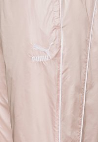 Puma-jacka i ljusrosa tyg, med en vit broderad logotyp och tunna vita accenter längs sömmarna. Slät textur, minimalistisk design.