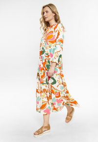 Maxikleid mit Blumenmuster, mehrlagig und langen Ärmeln in Creme, Orange, Grün, Pink und Blau. Kombiniert mit braunen Wedge-Sandalen.