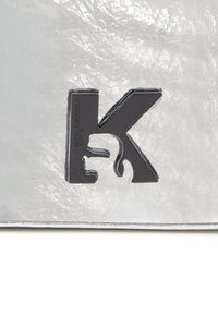 Hõbedane tekstuuriga pind, millel on silmapaistev must K-kiri külgprofiilis. Logol on tekst "Karl Lagerfeld Jeans."