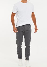 Męski strój składający się z białej bawełnianej koszulki, szarych slim fit spodni i białych sneakersów, z podwiniętymi mankietami i swobodnym krojem.