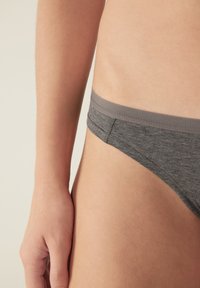 Grijze katoenen stringonderbroek met een gladde textuur en een lichtgrijze tailleband. Geknipt met minimale bedekking, waardoor het heupgebied zichtbaar is.