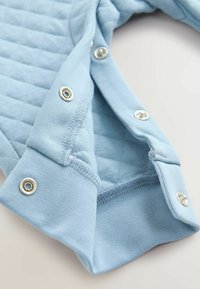 Svijetloplaka košulja dugih rukava s quiltanom teksturom i srebrnim gumbima na ovratniku. Pamuk s mekanim završetkom.