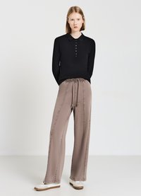 Schwarzes langärmliges Poloshirt mit Knopfleiste, kombiniert mit hellbeigen, weit geschnittenen Hosen mit elastischem Bund. Legere weiße Sneakers.