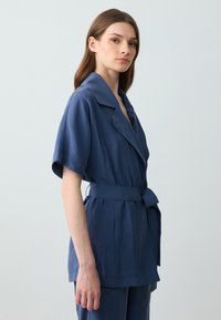 Navyblaue, mit Gürtel versehene Bluse aus leichtem Stoff, mit kurzen Ärmeln, weitem Kragen und lockerer Passform.