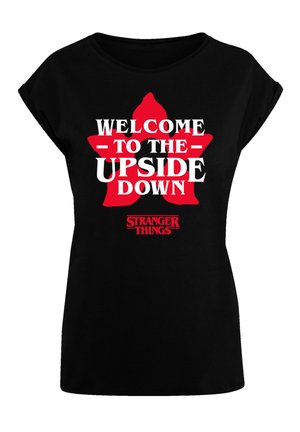 Zwart katoenen T-shirt met opvallende witte en rode tekst: "WELKOM IN DE UPSIDE DOWN" en het "STRANGER THINGS" logo onderaan. Korte mouwen.