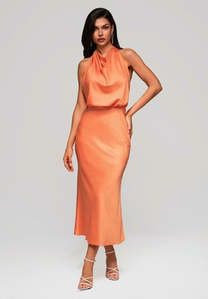Halter neck dress in soft orange fabric, featuring a draped bodice and a fitted skirt. Smooth texture with a mid-length design. Strappy heels.