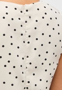 Κοντινή λήψη κρεμ υφάσματος με μαύρες πουά βούλες και λευκή ραφή φερμουάρ στο πίσω μέρος ενός αμάνικου ενδύματος.