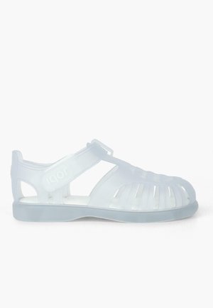 Transparent plastic sandals with open design, featuring cut-out patterns, adjustable strap, and a flat sole. Brand name "Igor" visible.