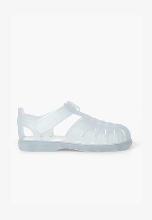 Transparent plastic sandals with open design, featuring cut-out patterns, adjustable strap, and a flat sole. Brand name "Igor" visible.