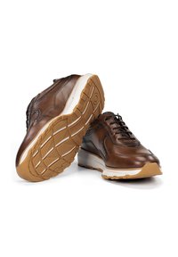 Zapatillas de cuero marrón con acentos estampados, punta redonda y suela de goma con un agarre texturizado. Se pueden ver los cordones y los detalles de costura.