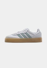 Sneaker bianca con strisce verde chiaro, punta in suede e suola in gomma texturizzata. Presenta lacci e brand sulla parte laterale. Design classico a basso profilo.