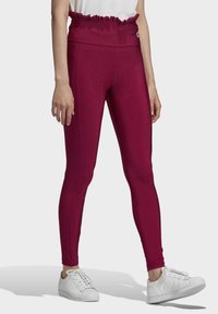 Korta, figurnära leggings i vinröd med en volangmidja, slät textur och sömdetaljer, tillsammans med vita sneakers.