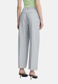 Pantalons larges gris clair avec une taille élastique, dotés de deux poches arrière et d'un tissu lisse et texturé.