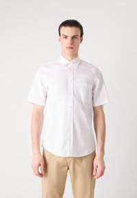 Camisa blanca de botones de manga corta en algodón, con cuello puntiagudo, un bolsillo en el pecho y un dobladillo curvado. Textura suave.