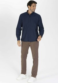 Chemise à manches longues bleue marine avec boutons, associée à un pantalon marron et des baskets blanches. La chemise possède un col et une texture lisse.