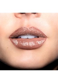 Lackfarbener Lippenstift mit glatter Textur, vollem Schwung und subtiler Schimmer; gut definierte Konturen und neutraler Unterton. Weiße Zähne sichtbar.