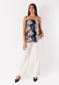 Top senza maniche con motivi floreali blu e beige; realizzato in tessuto liscio. Abbinato a pantaloni a gamba larga color crema e tacchi a punta neri.