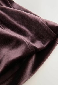 Donkerpaarse fluwelen stof, zachte textuur, gladde glans, met zichtbare naden en plooien. De vorm is gedrapeerd, waardoor de vloeibaarheid van het materiaal wordt getoond.