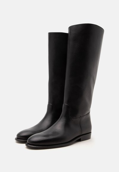 Bottes hautes en cuir noir avec un bout arrondi et un talon bas, debout côte à côte sur fond blanc.