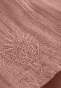 Textilmerkmal: weicher, pinkfarbener Stoff mit gesticktem Sonnenmotiv und subtilen strukturierten Linien, die ein zartes, geschichtetes Aussehen erzeugen.
