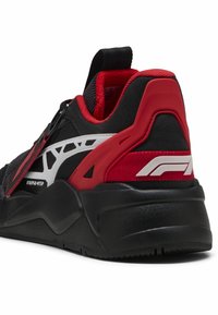 Chaussure de sport noire et rouge avec une tige texturée, des accents blancs, et une semelle coussinée, présentant des superpositions détaillées et un design de talon proéminent.